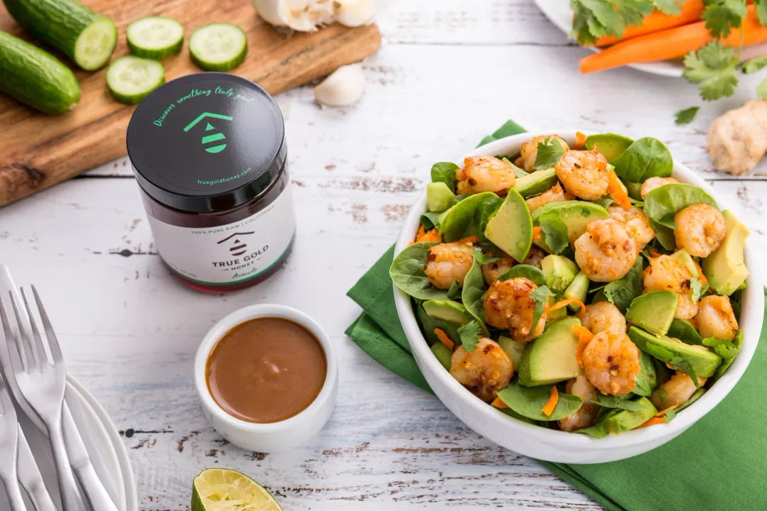 Salad with shrimp and greens on a white plate, accompanied by a jar of dressing and cut vegetables.