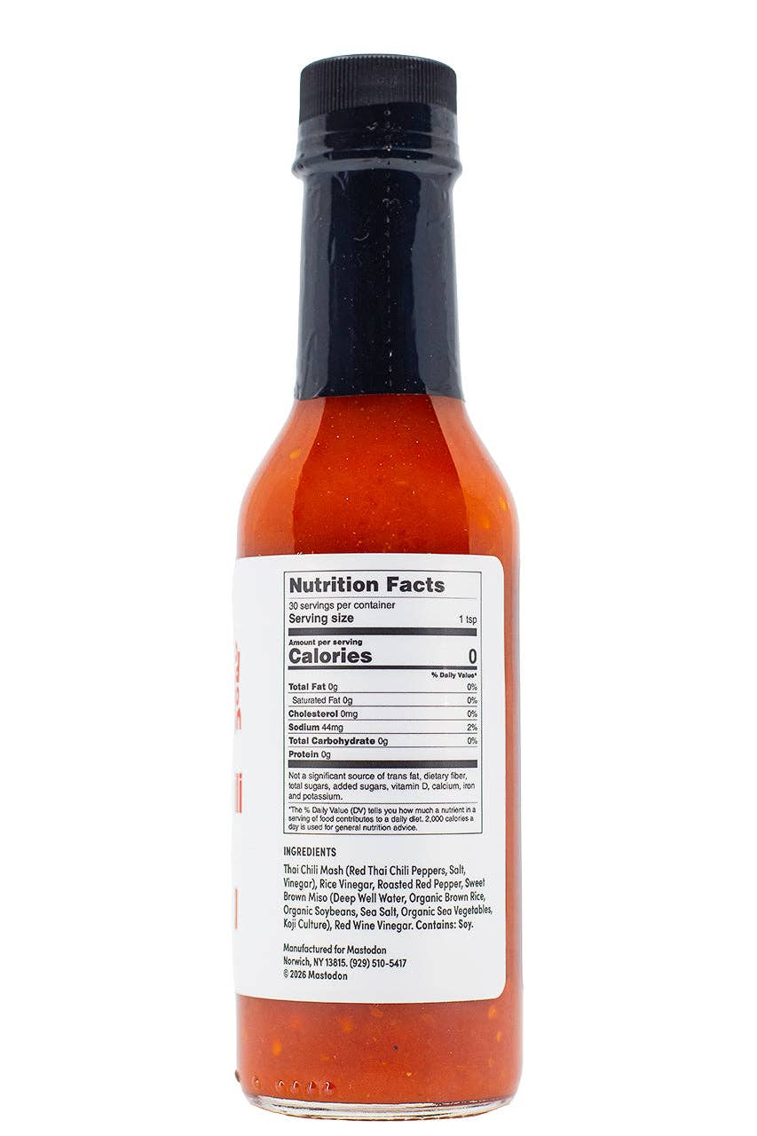 A bottle of hot sauce shown from the back, featuring a black cap, clear glass bottle, vibrant orange-red sauce inside, and a white nutrition facts label on a white background.