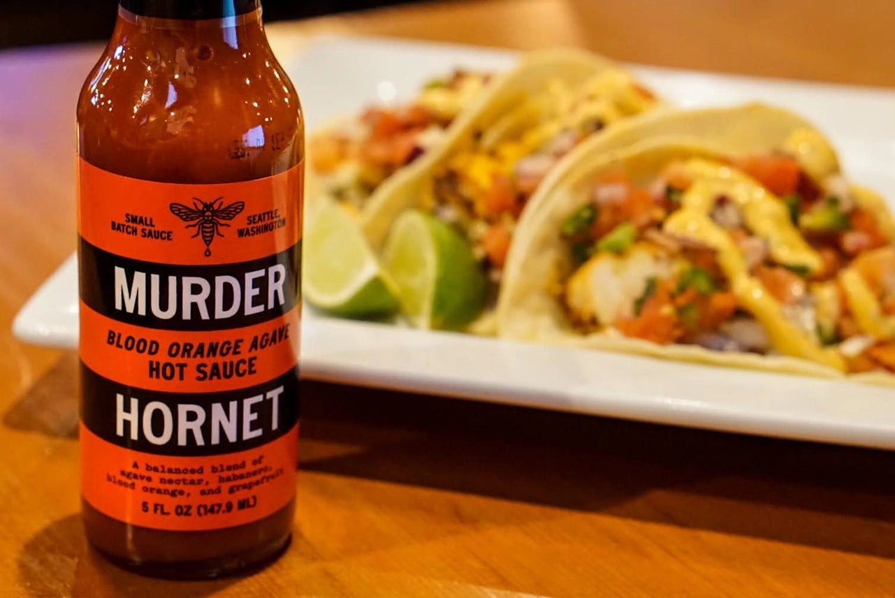 Bottle of Murder Hornet hot sauce next to tacos on a plate