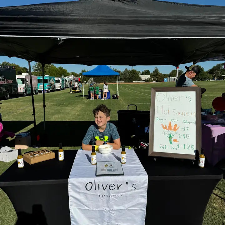 Oliver at a hot sauce stand with a sign and his hot sauce under a black tent