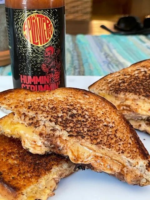 Grilled cheese sandwich with a bottle of Splintered Hummin Strummin hot sauce on a table.