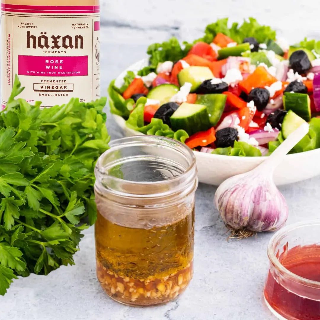 Haxan rose wine bottle with a jar of olive oil, garlic, and a salad on a marble surface.
