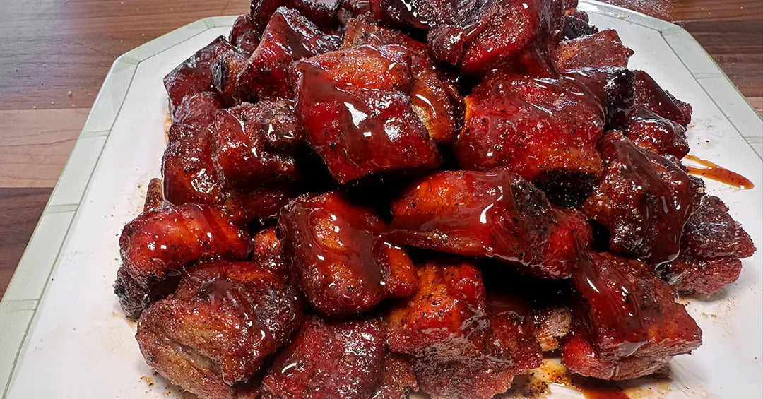 Platter of glossy red-brown meat chunks on a wooden surface