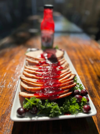 Platter of sliced meat with cranberry sauce on a wooden table, featuring a bottle in the background.