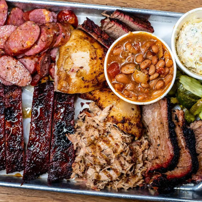 Platter of barbecue meats including ribs, brisket, and chicken, with sides of baked beans and coleslaw.