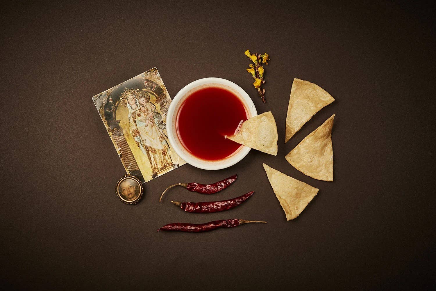 Tea cup with red liquid, tortilla chips, dried chili peppers, and a card on a brown background