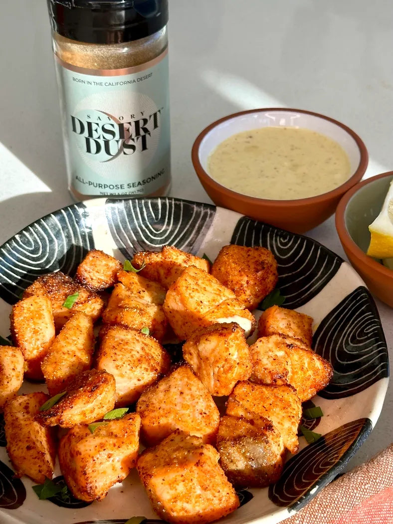 Plate of seasoned croutons with a bottle of 'Desert Dust' seasoning and a bowl of dipping sauce.