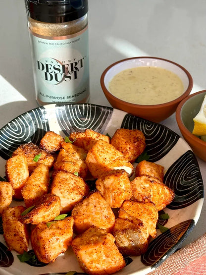 Plate of seasoned croutons with a bottle of 'Desert Dust' seasoning and a bowl of dipping sauce.