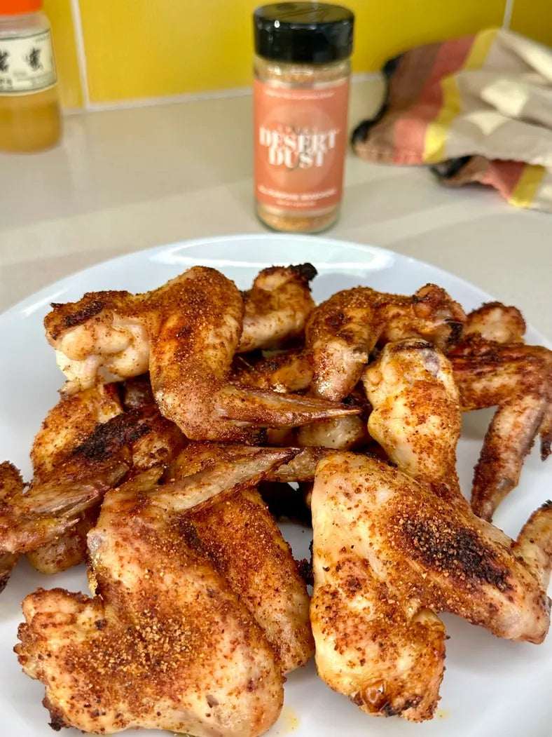 Spiced chicken wings on a white plate with a bottle of seasoning in the background.