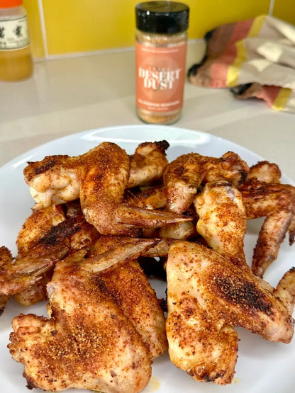 Spiced chicken wings on a white plate with a bottle of seasoning in the background.