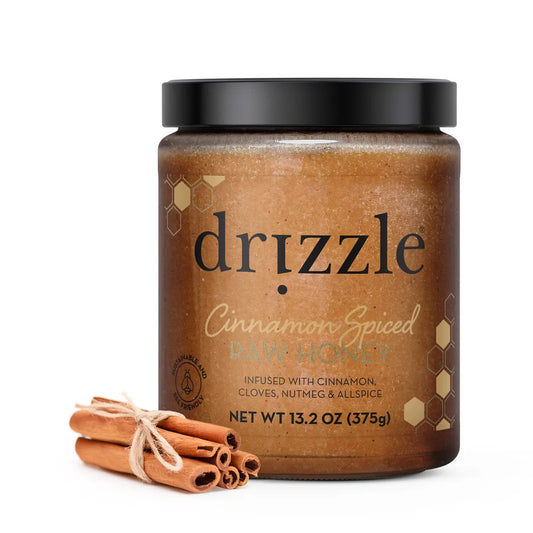 Jar of drizzle cinnamon spiced raw honey with cinnamon sticks on a white background