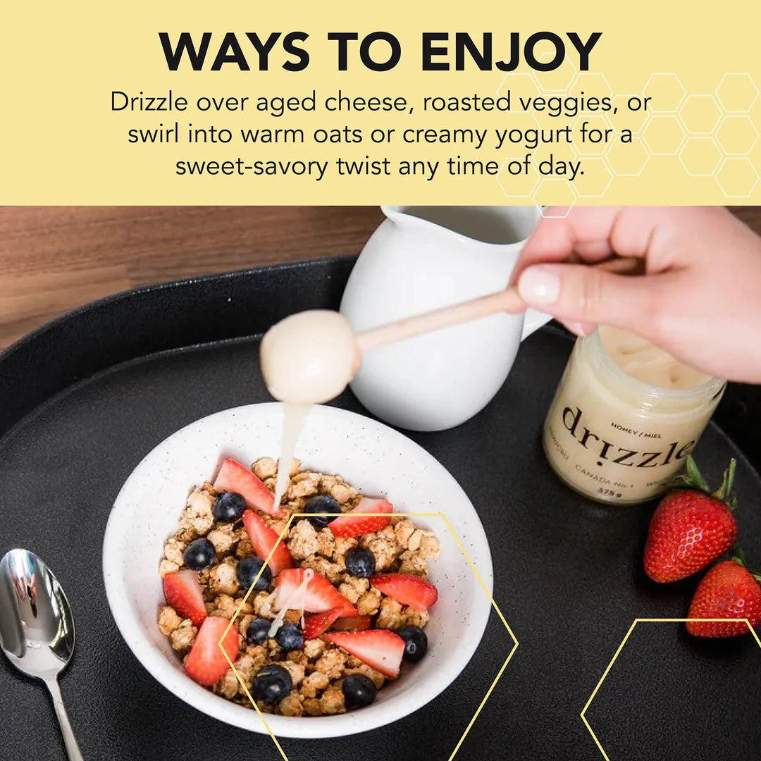 Drizzling White Honey over a bowl of cereal with strawberries and blueberries on a black tray.