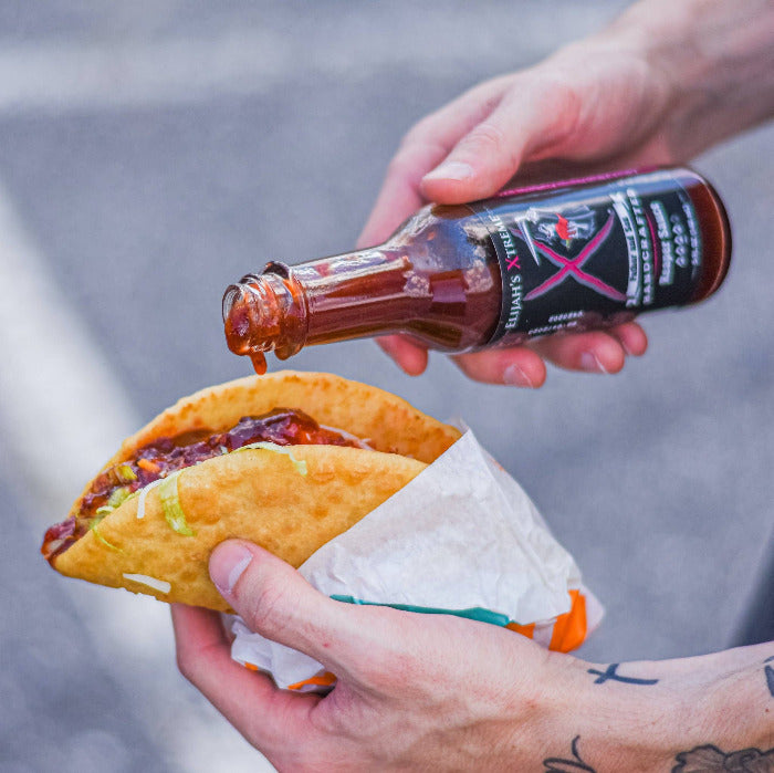 Person pouring sauce from a bottle onto a taco