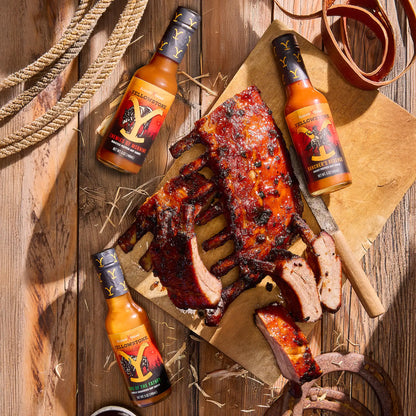 Grilled ribs with three bottles of hot sauce on a wooden surface