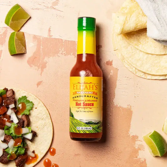 Bottle of Eliah's hot sauce with a taco and lime wedges on a textured surface
