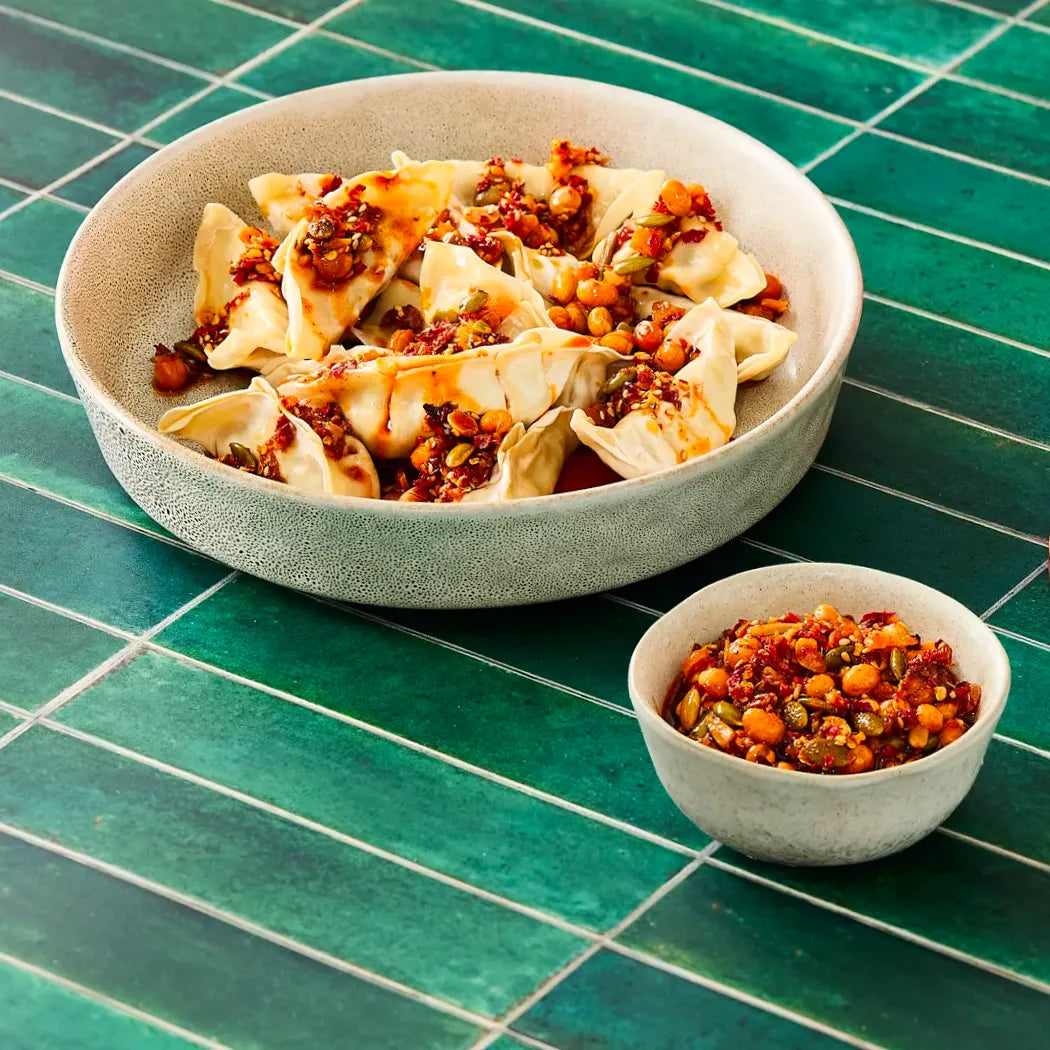 Bowl of dumplings with crunchy chili crisp with a side dish on a green tiled surface