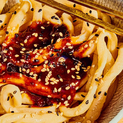 Noodles with a dark sauce and sesame seeds on a wooden plate