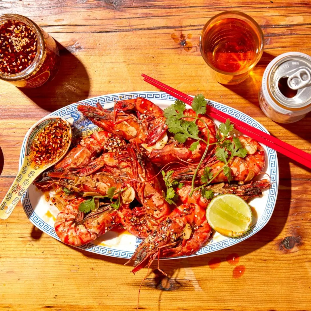 Platter of spicy prawns with a can of beer and a glass of beer on a wooden table.