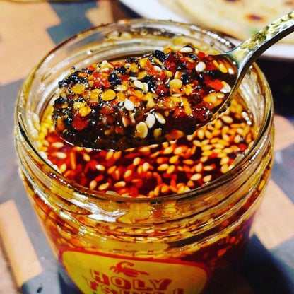 Jar of spicy sauce with a spoonful being lifted, on a wooden surface.