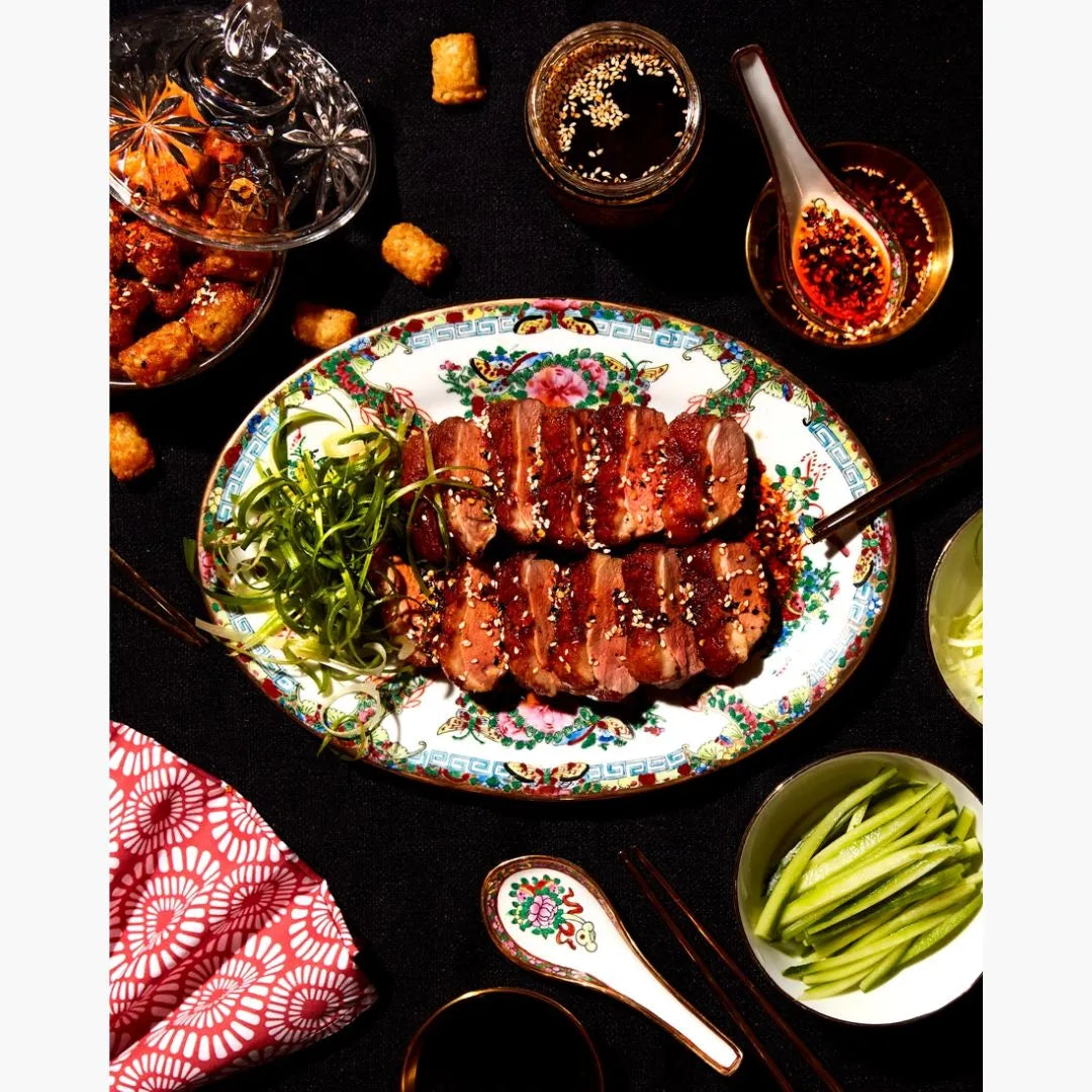 Decorative plate with roasted meat, garnished with green vegetables on a dark surface.