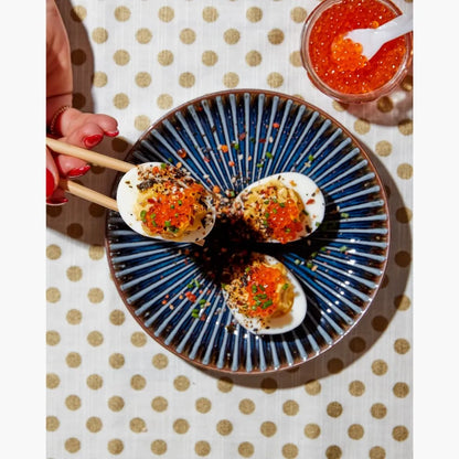 Deviled eggs with salmon roe on a blue plate with a polka dot tablecloth.