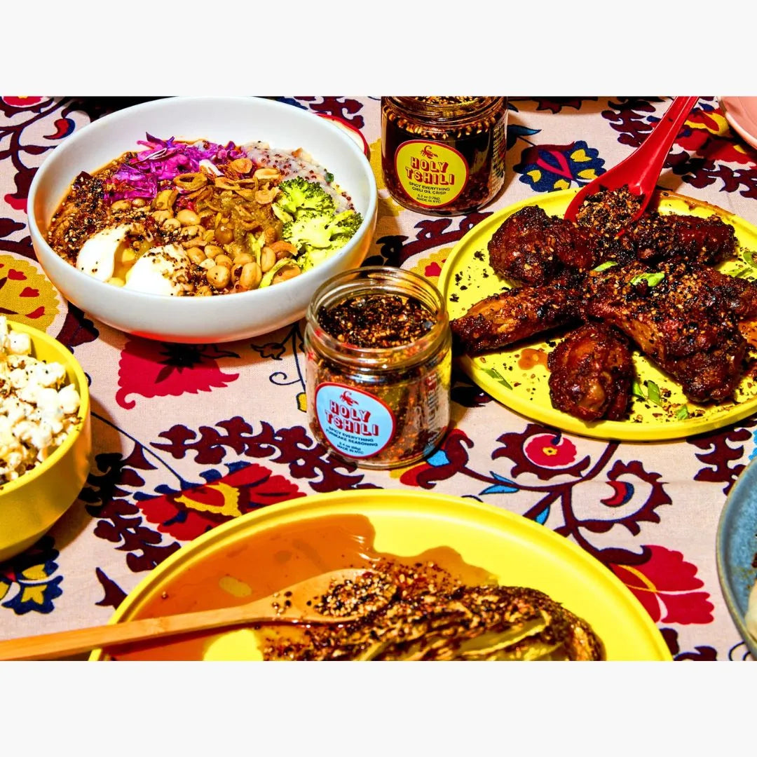 Diverse food items including a bowl of salad, plates of meat, and popcorn on a patterned tablecloth.
