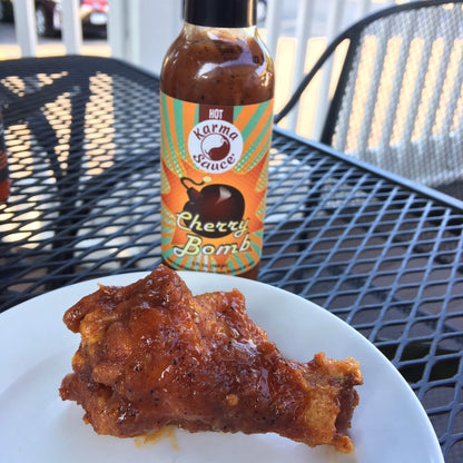 Bottle of Karma Sauce Cherry Bomb with a fried chicken wing on a plate outdoors.