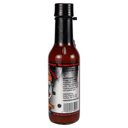 Back view of a hot sauce bottle on a plain white background, showing the label text and barcode. The bottle contains a dark reddish-brown sauce and has a black cap.