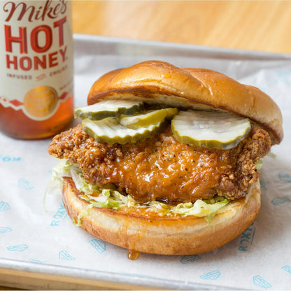 Burger with fried chicken, pickles, and lettuce on a bun next to a bottle of Mike's Hot Honey.