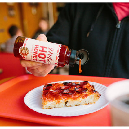 Person pouring hot honey over a slice of pizza on a red tray.