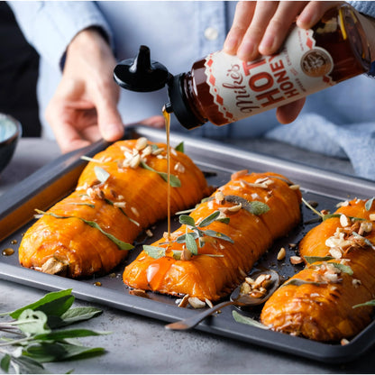 Person drizzling hot honey over roasted sweet potatoes on a baking tray.