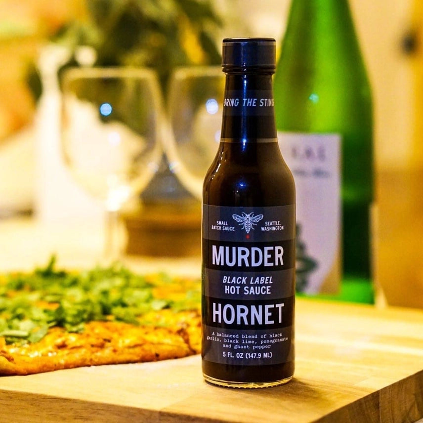 Bottle of Murder Hornet Black Label Hot Sauce on a table with a blurred background