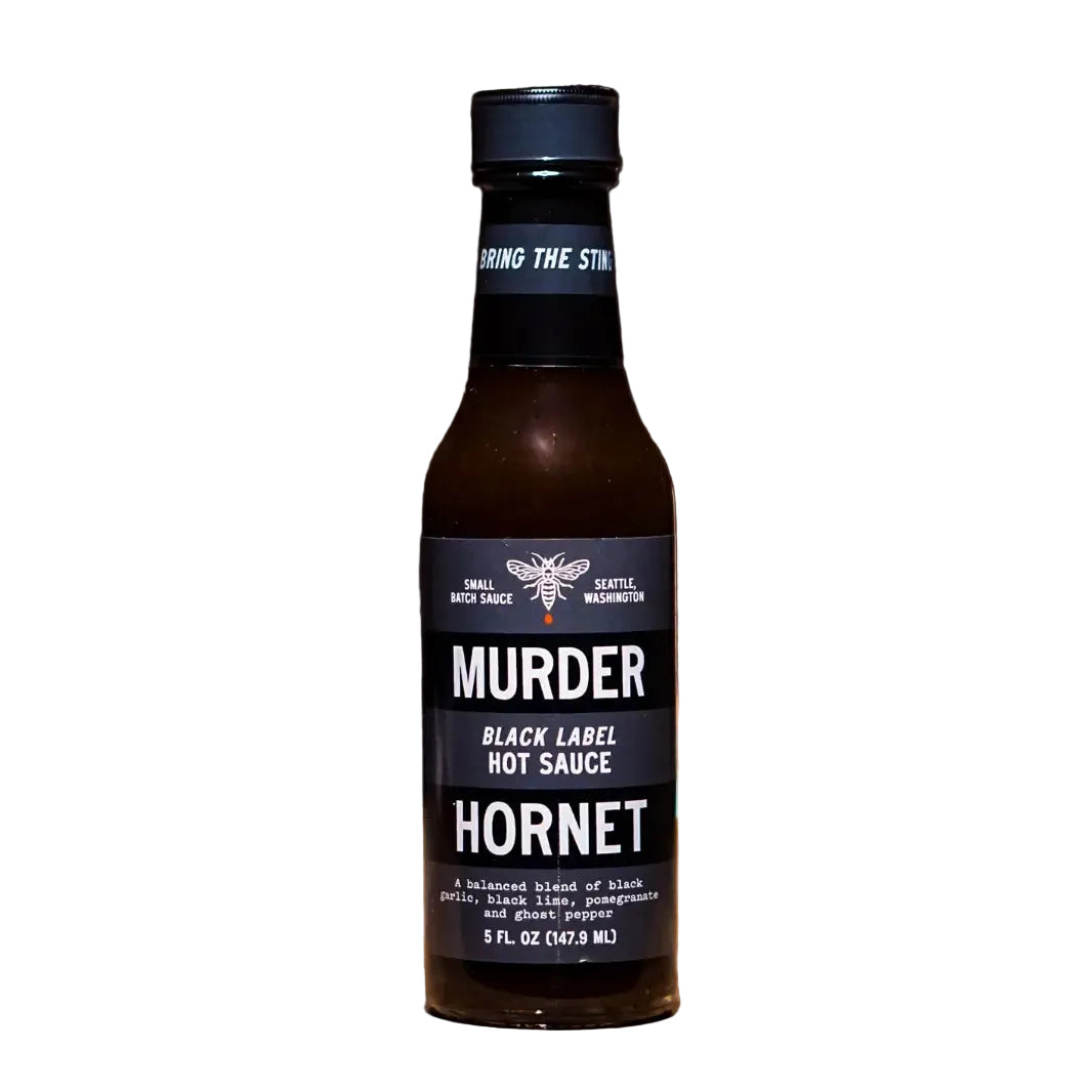 Bottle of Murder Hornet Black Label Hot Sauce on a wooden surface with 'Great Taste' award logo.