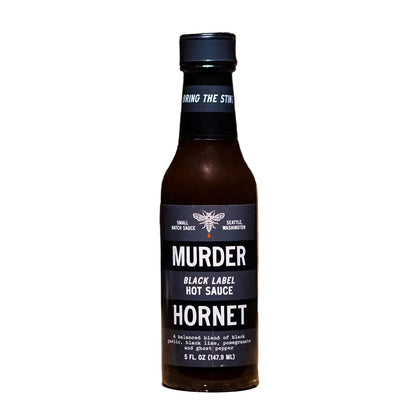 Bottle of Murder Hornet Black Label Hot Sauce on a wooden surface with 'Great Taste' award logo.
