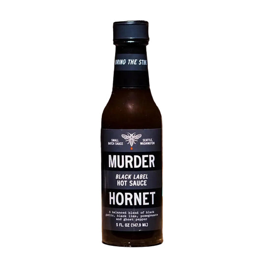 Bottle of Murder Hornet Black Label Hot Sauce on a wooden surface with 'Great Taste' award logo.