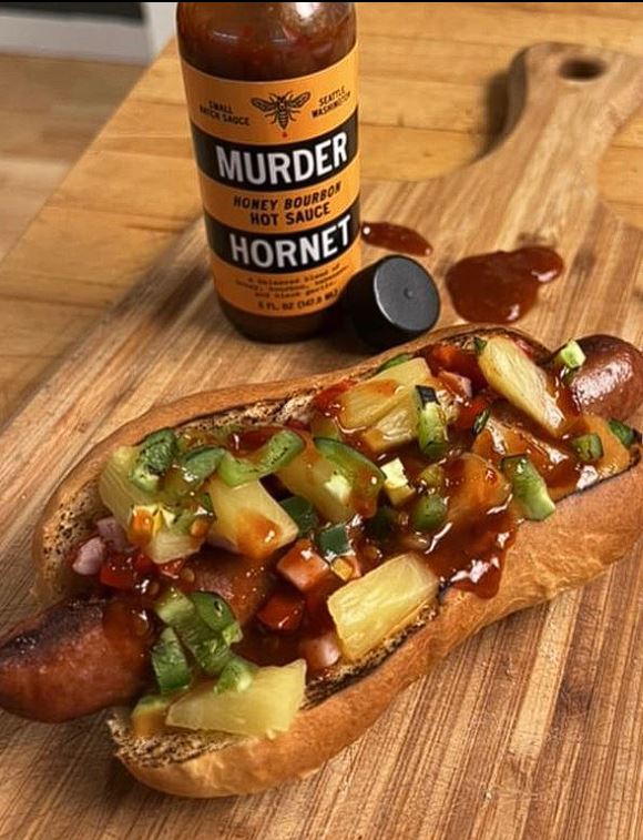Murder Hornet Honey Bourbon Hot Sauce on a hot dog and bun with toppings