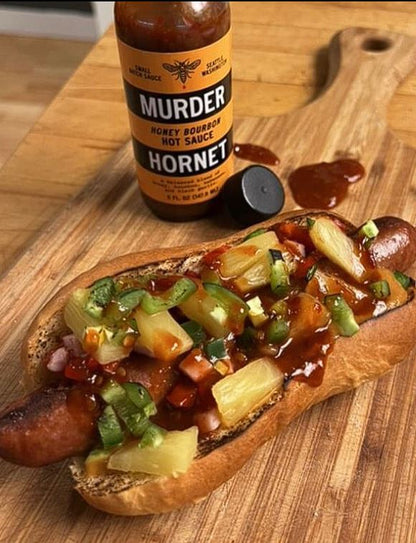 Murder Hornet Honey Bourbon Hot Sauce on a hot dog and bun with toppings