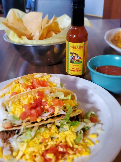 Tacos with cheese and tomatoes on a plate with a bottle of salsa in the background.