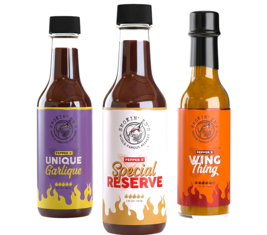 Three bottles of Smokin Ed's Pepper X hot sauce with colorful labels on a white background
