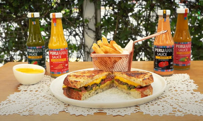 Grilled cheese sandwich on a plate with fries and Peruvian sauce bottles on a wooden table.