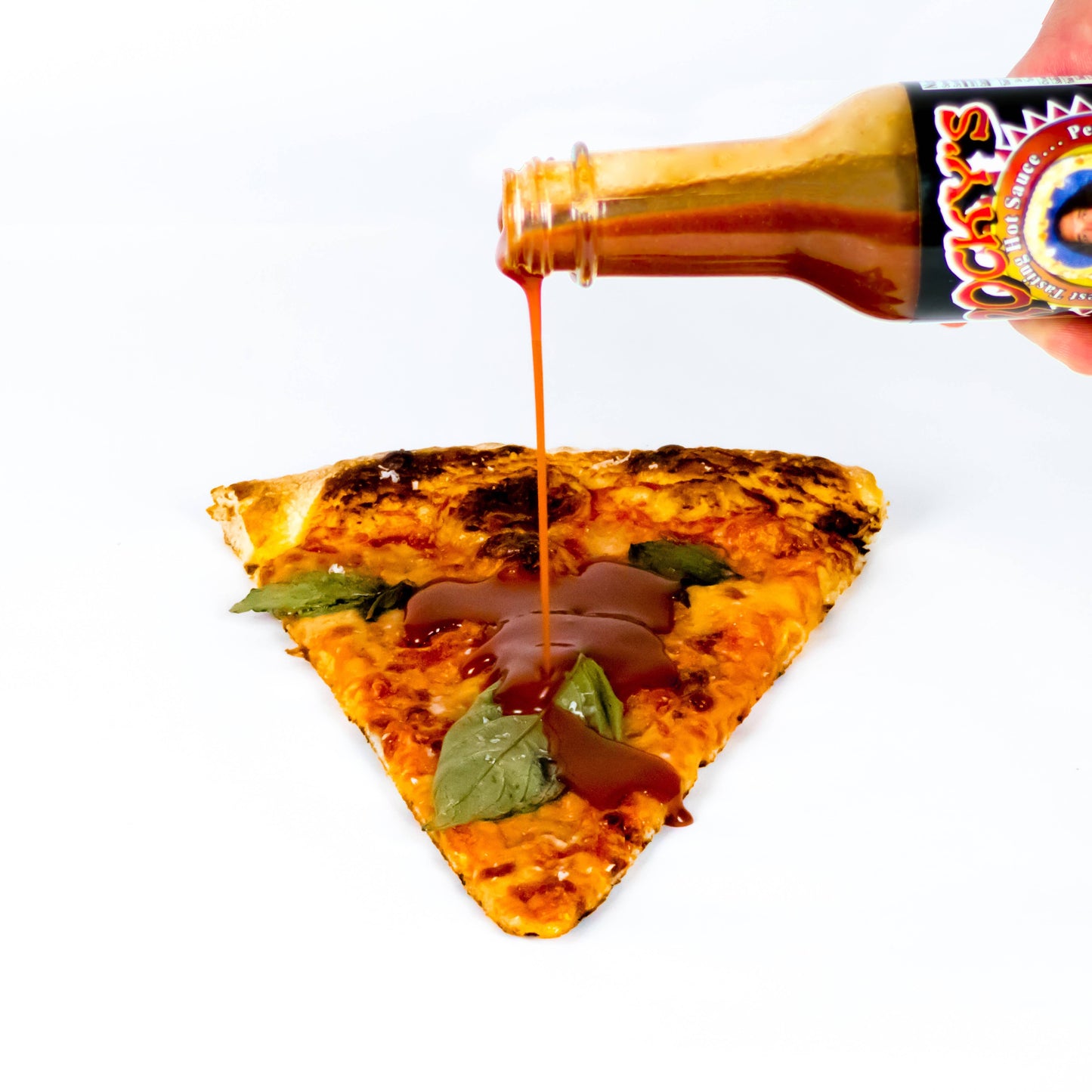 Pizza slice with a bottle of Rocky's Nashville hot sauce being poured over it on a white background