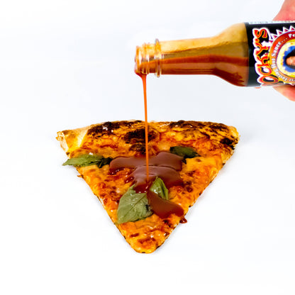 Pizza slice with a bottle of Rocky's Nashville hot sauce being poured over it on a white background