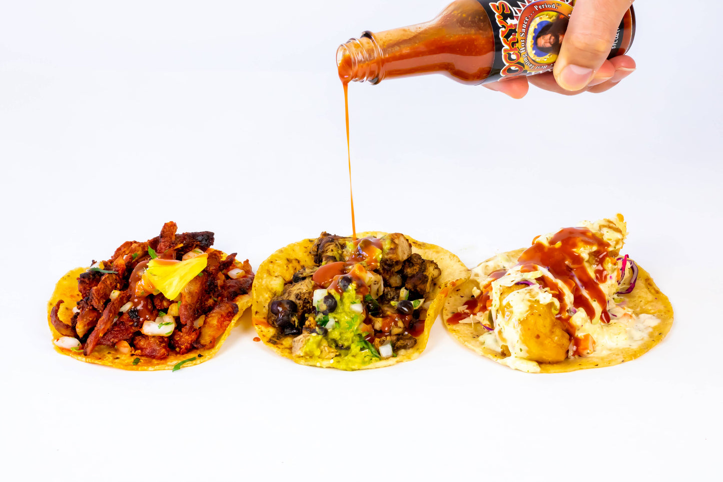 Three tostadas being drizzled with Rocky's Nashville hot sauce from a bottle on a white background