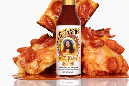 Bottle of honey hot sauce with a pizza in the background
