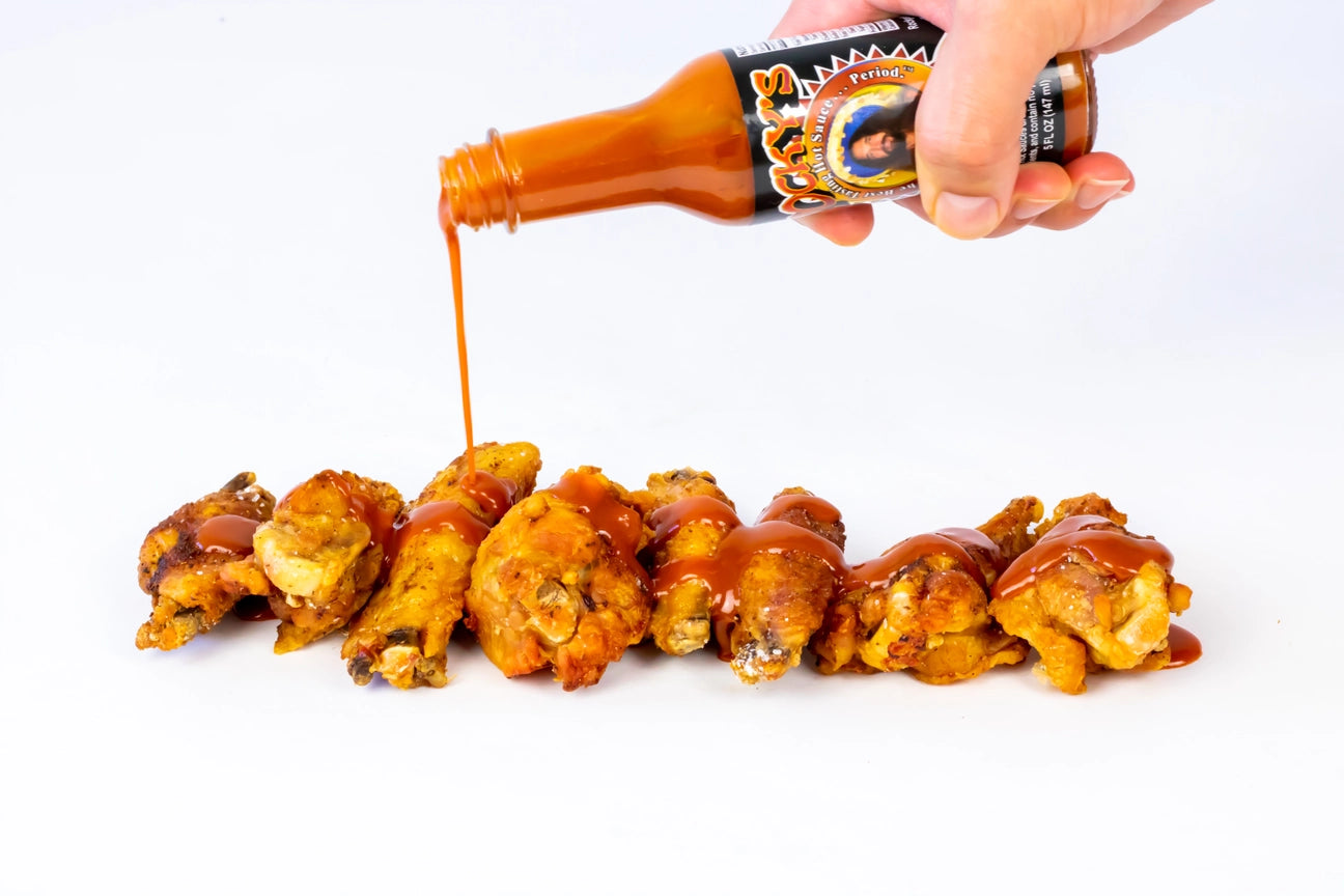 Hot sauce being poured onto chicken wings on a white background