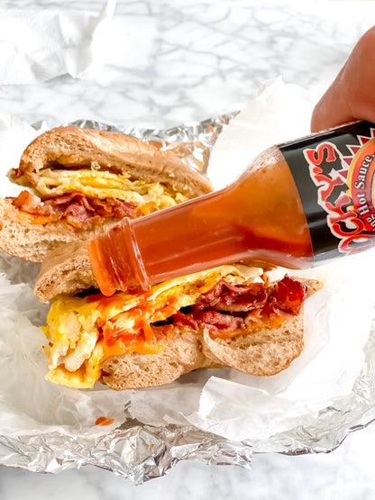 Hot sauce being poured onto a sandwich on crumpled paper