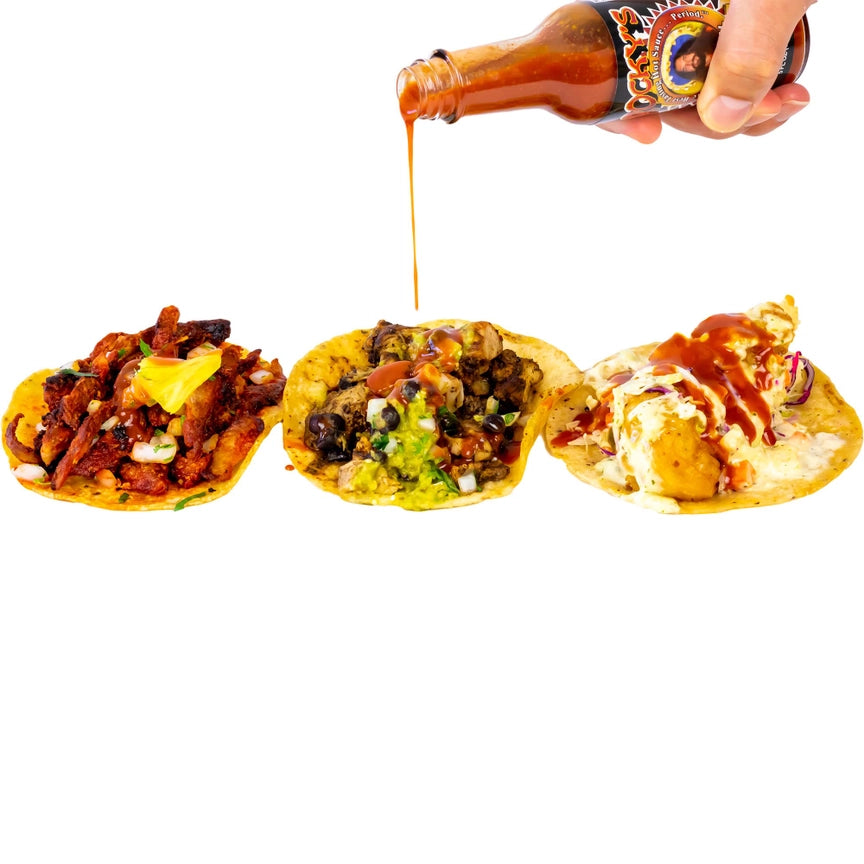 Three types of tacos being drizzled with hot sauce from a bottle on a white background