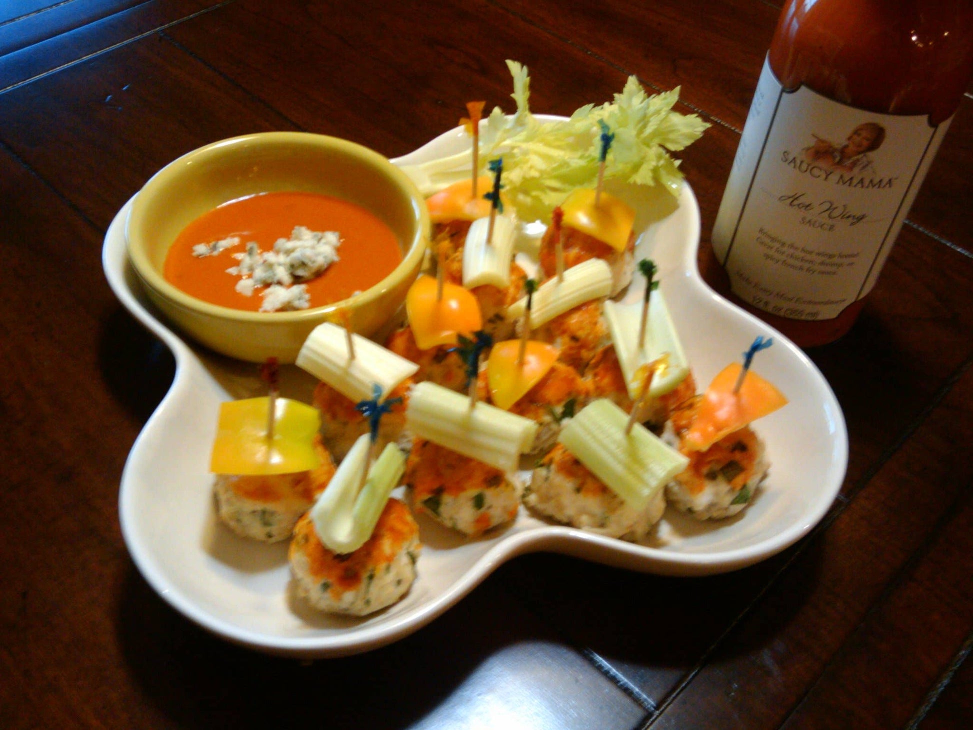 Platter of appetizers with a bowl of soup and a bottle of Saucy Mama hot sauce on a wooden table.