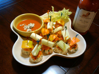 Platter of appetizers with a bowl of soup and a bottle of Saucy Mama hot sauce on a wooden table.