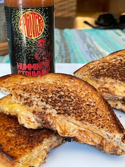 Grilled cheese sandwich with a bottle of Splintered Hummin Strummin hot sauce on a table.